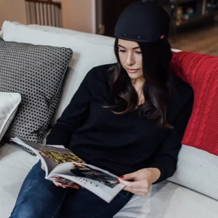 Woman comfortably wearing REVIAN Red cap while reading on a sofa